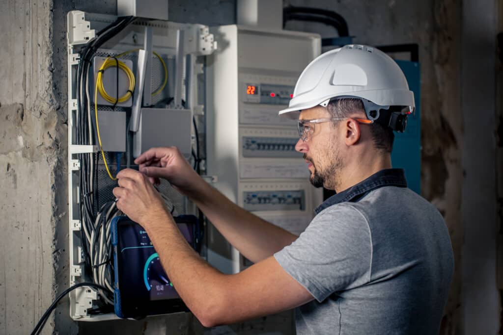 man, an electrical technician working in a switchboard with fuses, uses a tablet.